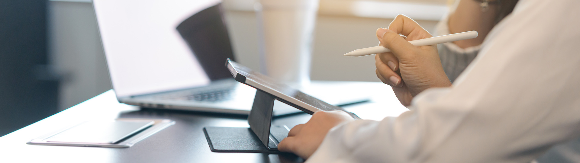 Two young business women sitting at table. First woman holding stylus pen with digital tablet screen. close up side view.