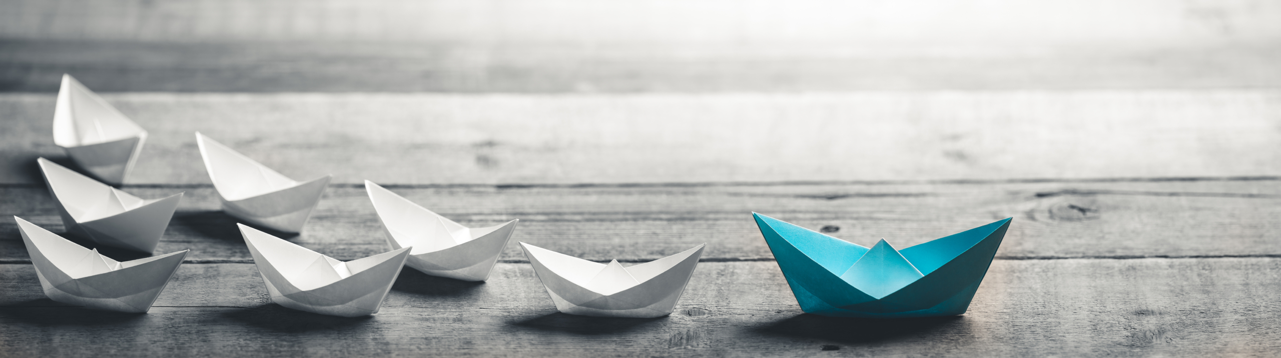 Blue Paper Boat Leading A Fleet Of Small White Boats On Wooden T